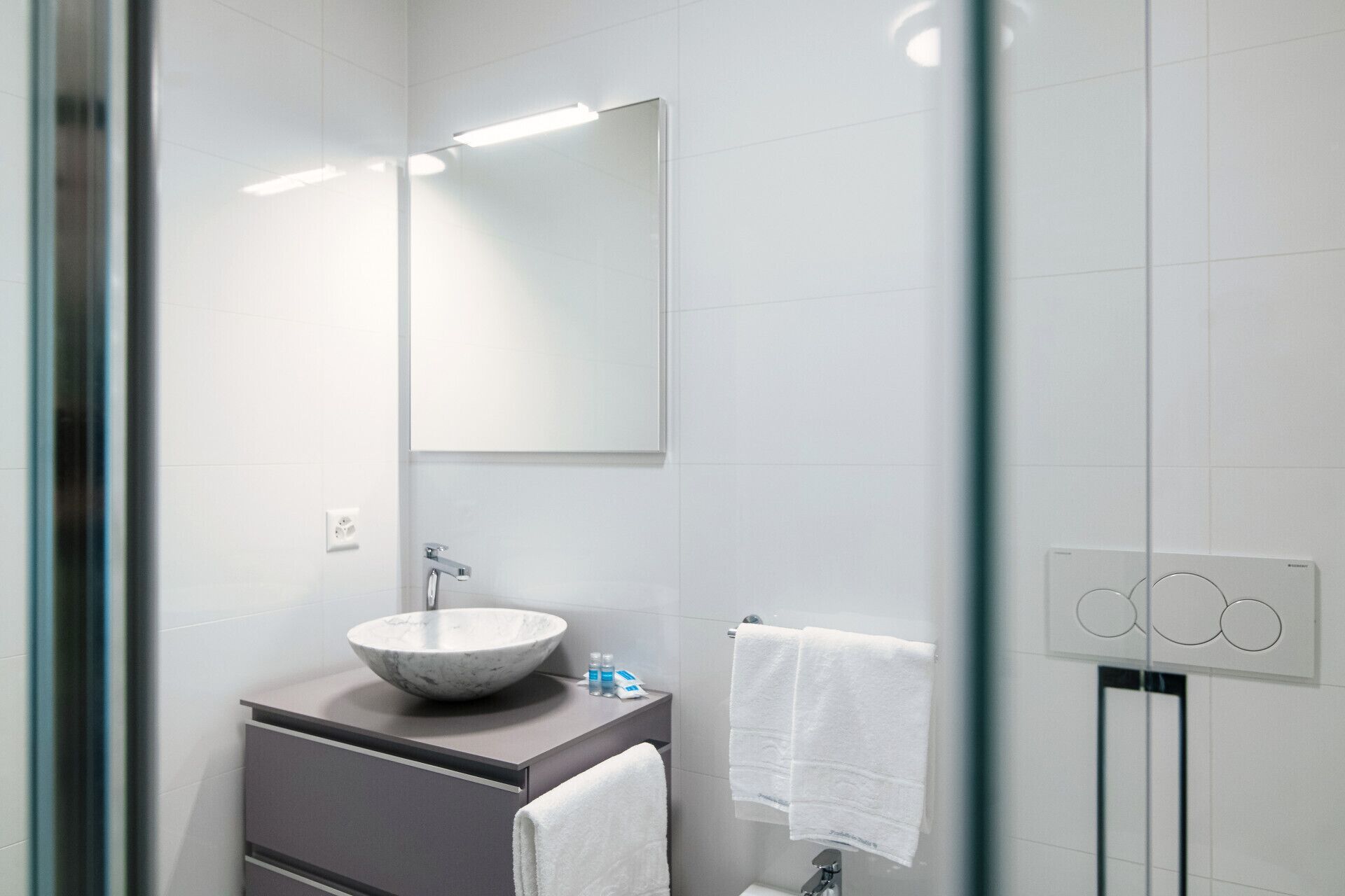 Un baño moderno con un espejo grande, un lavabo redondo de mármol y un perchero para toallas.