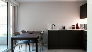 A modern kitchen with a dark countertop, a kettle, a red appliance, and a window overlooking a garden. - Studio with balcony near the center of Locarno (YELLOW STUDIO 12) (Locarno)