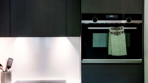 A kitchen with a digital clock displaying 09:23, a green oven mitt hanging on the oven handle, and a utensil holder with spatulas and a spoon. - Studio with balcony near the center of Locarno (YELLOW STUDIO 12) (Locarno)