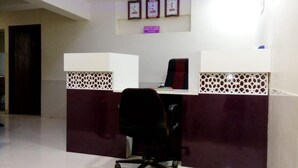 Un mostrador de recepción con una silla de oficina negra, un reloj en la pared y un cartel sobre el mostrador.
