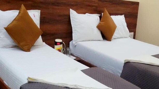 Dos camas individuales con cabeceros de madera, ropa de cama blanca y almohadas marrones.