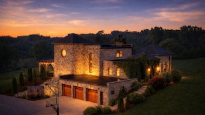 A stone house with a garage, a covered porch, and a well-lit driveway at dusk. - Stay in a Real Castle on a Vineyard (Cleveland)