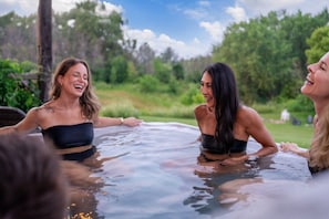 Drie personen in een bubbelbad, buiten, omringd door groen.