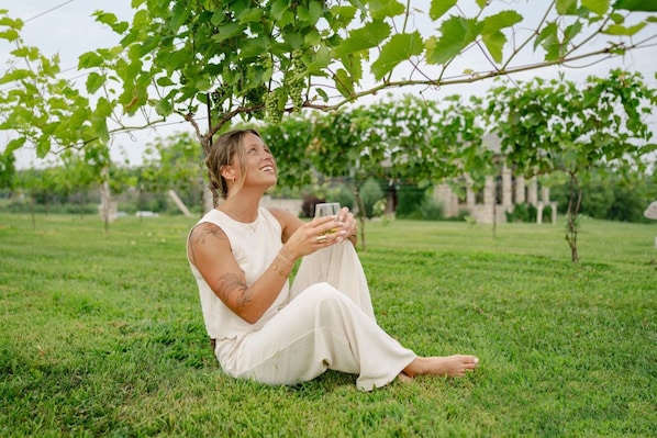 A person sitting on grass under a tree with a glass of drink.