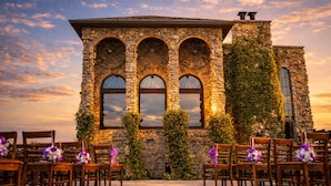 A stone building with arched windows and ivy-covered walls, surrounded by wooden chairs and tables. - Stay in a Real Castle on a Vineyard (Cleveland)