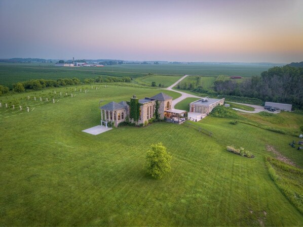 A large estate with a main building and several smaller structures, surrounded by expansive green fields.