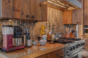 Een keuken met houten kastjes, een roestvrijstalen fornuis en diverse apparaten, waaronder een koffiezetapparaat en een blender.