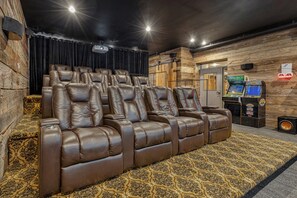 Een bioscoopkamer met leren loungestoelen, een kamerbreed tapijt met dessin en arcade spelautomaten.
