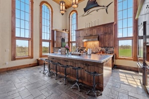 A spacious kitchen with a large island, bar stools, and a view of the outdoors.