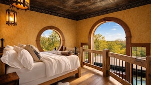 A bedroom with a large bed, two windows, a wooden railing, and a view of trees. - Stay in a Real Castle on a Vineyard (Cleveland)