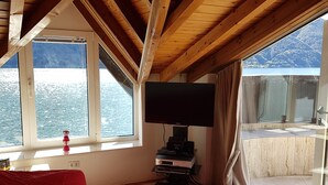 A room with a red sofa, a flat-screen TV, and a balcony with a view of a snowy landscape. - Directly on Lago di Lugano with boat mooring (Porlezza)