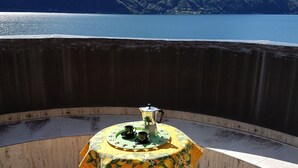 A table with a floral tablecloth on a balcony overlooking a body of water and mountains. - Directly on Lago di Lugano with boat mooring (Porlezza)