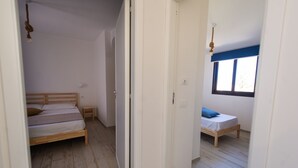A narrow hallway with two bedrooms, each with a wooden bed and a small bedside table.