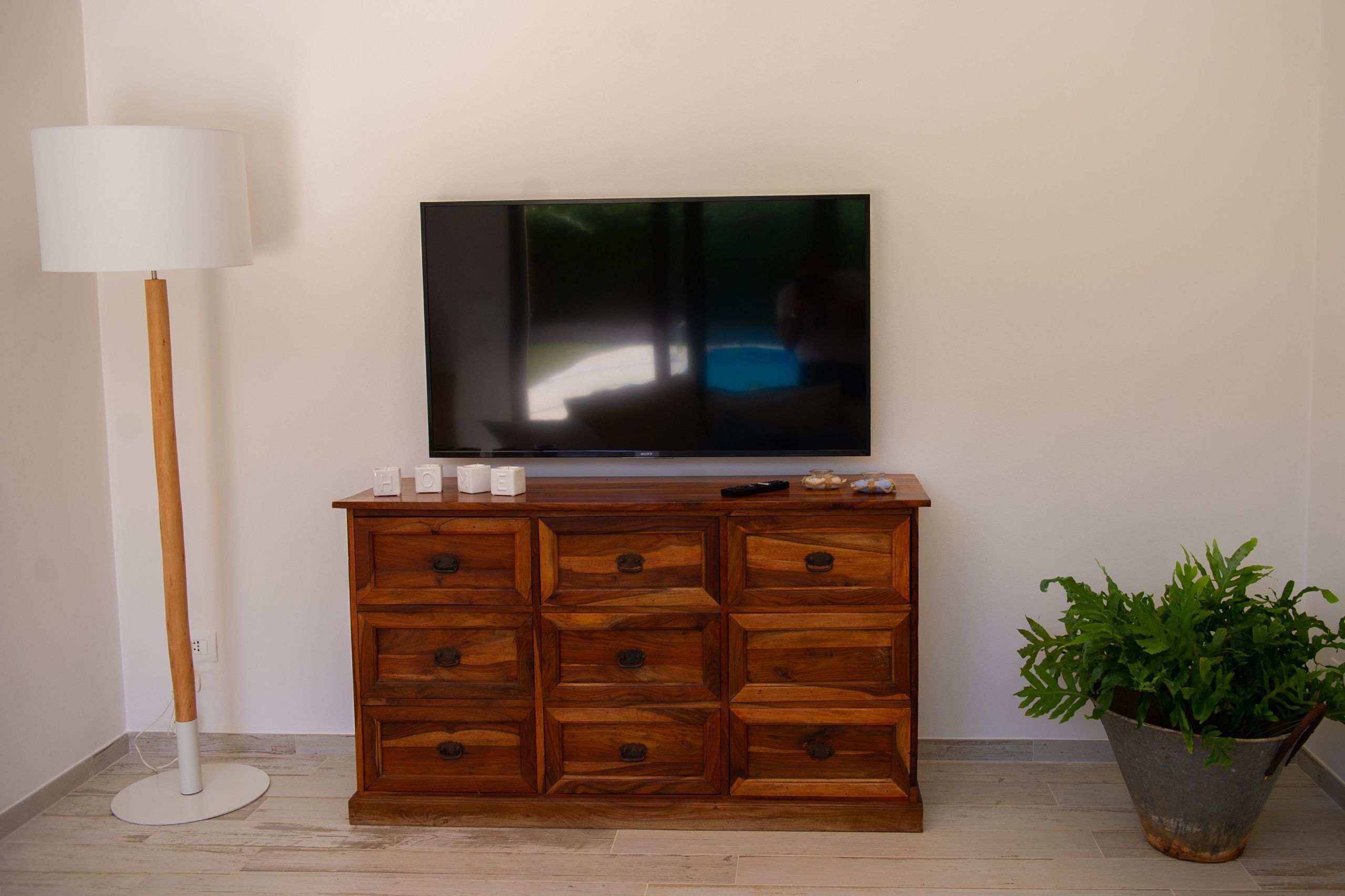 A wooden cabinet with drawers, a flat-screen TV on top, a floor lamp, and a potted plant.