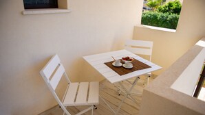 A small dining area with a white table and chairs, a bowl of fruit, and a view of greenery through a window. - LANDLORD TIPINO (Pizzolungo)