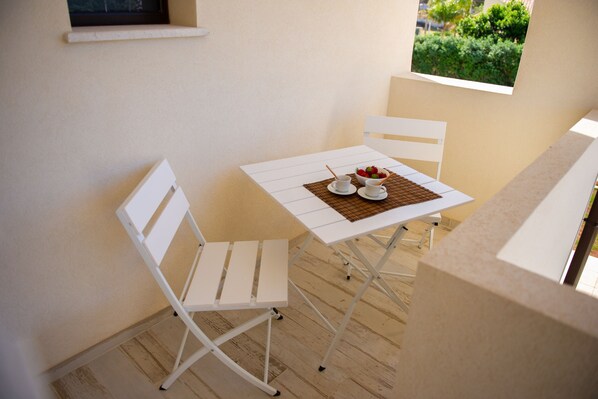 A small dining area with a white table and chairs, a bowl of fruit, and a view of greenery through a window. - LANDLORD TIPINO (Pizzolungo)