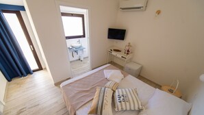 Une chambre d’hôtel avec un lit, un bureau doté d’un téléviseur à écran plat, une fenêtre et une salle de bain visible à travers une porte ouverte.