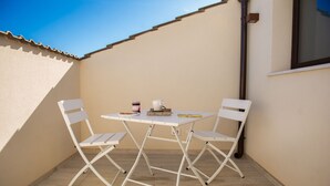 Une petite terrasse extérieure avec une table blanche et deux chaises blanches, un livre et une tasse posés sur la table.