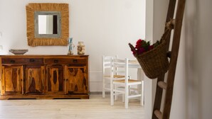 Une pièce avec un meuble en bois, des chaises blanches, un miroir et une échelle appuyée contre le mur.
