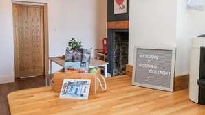 Un interior acogedor de cabaña con piso de madera, una mesa con una cesta de aperitivos, una chimenea y un cartel de bienvenida.