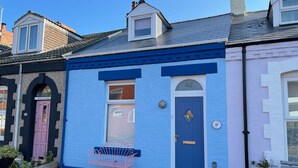 Una cabaña azul con puerta azul, una ventana pequeña y una puerta rosa, con el número 46 en la puerta.