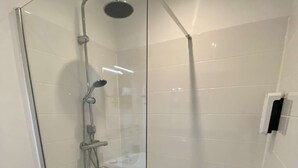 Une douche fermée par des parois en verre, dotée d’un pommeau de douche à main et d’un robinet mural.
