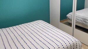 Une chambre à coucher avec un lit, des murs de couleur turquoise, un plafond blanc et un meuble avec une porte-miroir.