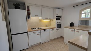 Une cuisine de taille réduite, dotée de meubles blancs, d’une cuisinière à gaz, d’un four à micro-ondes et d’un four traditionnel.