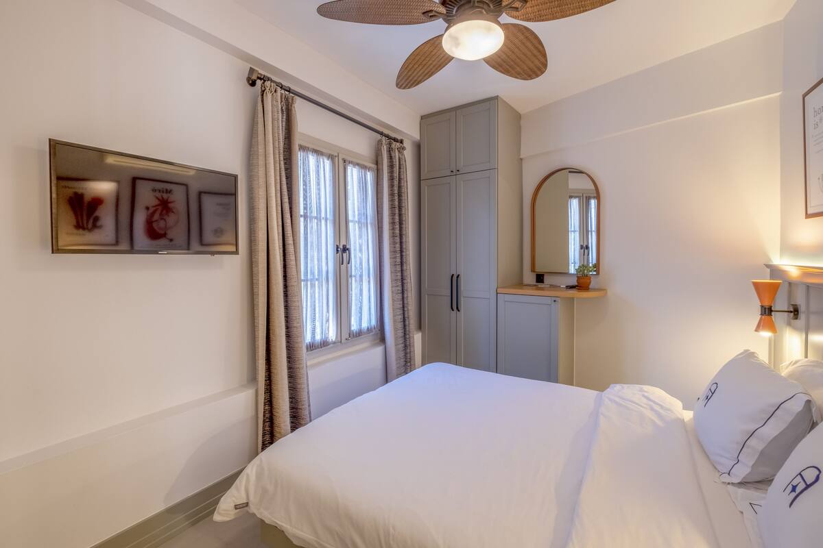A bedroom with a bed, a ceiling fan, a wardrobe, a mirror, and a framed picture on the wall.