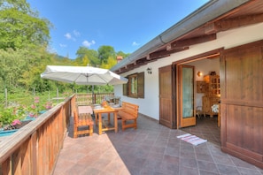 A wooden deck with a table and bench, an umbrella, and a view of a garden. - Casa Tra Borgo e Lago in Lake Tenno (Tenno)