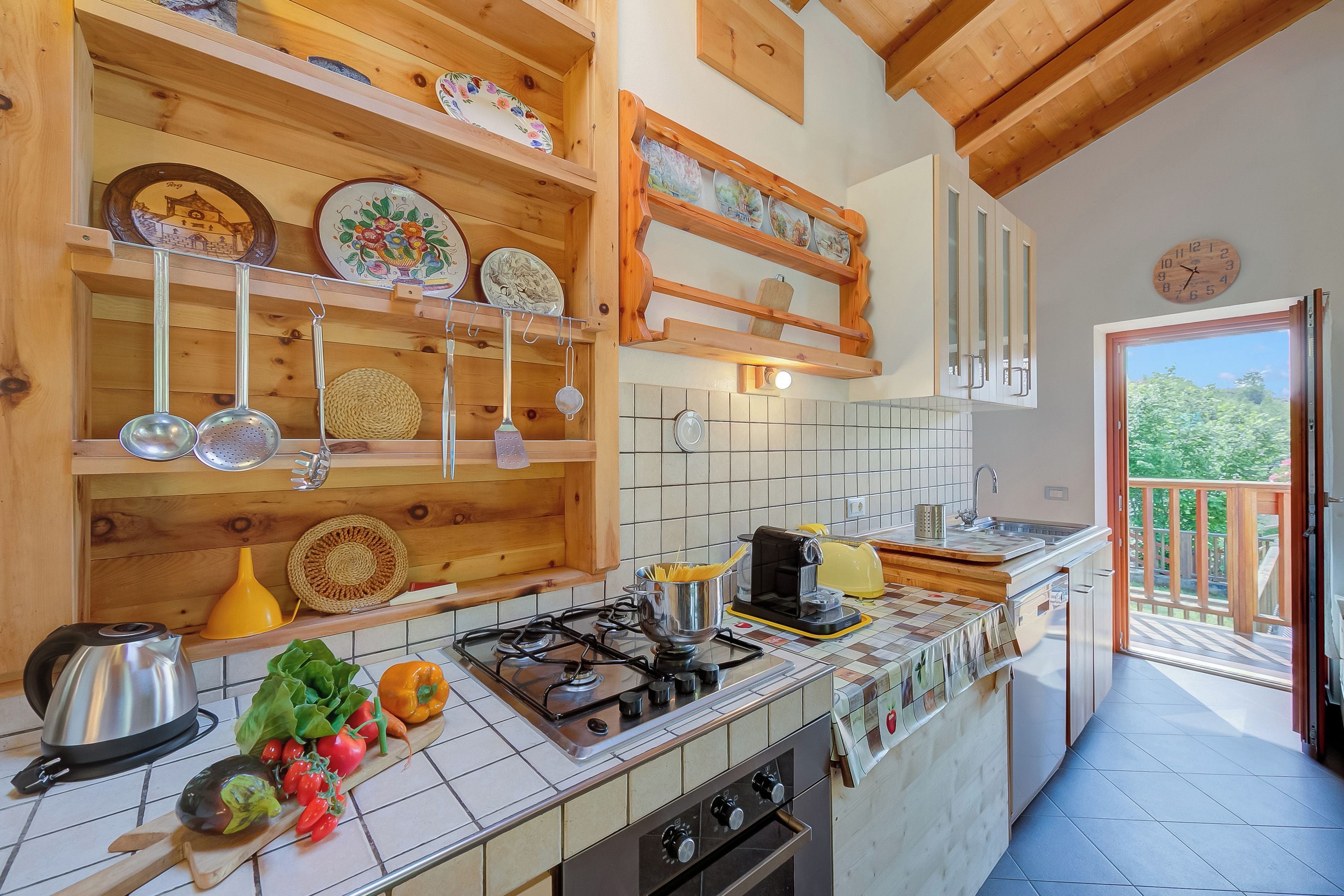 A kitchen with wooden shelves, a gas stove, and a view to the outside.