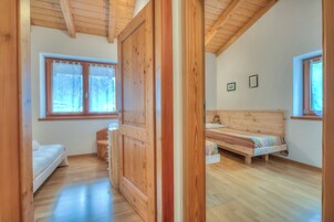 A wooden-floored room with two beds, a wooden wardrobe, and a window with a view of trees.