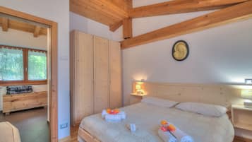 A bedroom with a wooden ceiling, a bed with white bedding and towels, a nightstand with a lamp, and a wardrobe.