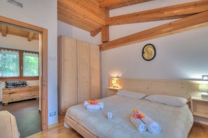 A bedroom with a wooden ceiling, a bed with white bedding and towels, a nightstand with a lamp, and a wardrobe. - Casa Tra Borgo e Lago in Lake Tenno (Tenno)
