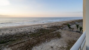 A beach view from a balcony with a clear sky, sandy beach, and sparse vegetation. - Beautiful Two Bedroom Oceanfront Great Mid Town Location! (Ocean City)