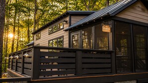 A cabin with a porch, large windows, and a deck. - Wildwood Den at The Retreat at Water's Edge (Tracy City)