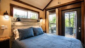 Een slaapkamer met een groot bed, een houten hoofdbord, twee bedlampjes en uitzicht op de omgeving door een schuifdeur.