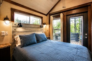 Une chambre à coucher avec un grand lit, une tête de lit en bois, deux lampes de chevet et une vue sur l’extérieur grâce à une porte coulissante.