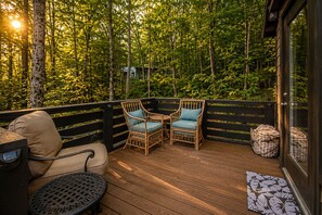 Une terrasse en bois, avec des chaises et un canapé en osier, entourée d’arbres.