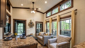 A spacious living area with a large window, a ceiling fan, and a cozy seating arrangement. - Wildwood Den at The Retreat at Water's Edge (Tracy City)