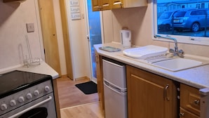 Kompakti keittiö, jossa on puiset kaapit, sisäänrakennettu uuni, jääkaappi ja ikkuna, josta on näkymä parkissa oleviin autoihin.