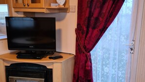 Huoneessa on televisio, takka, puukaapit ja punainen verho.