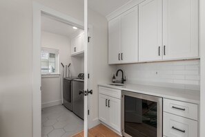 Een moderne keuken met witte kasten, een roestvrijstalen spoelbak en een raam met jaloezieën.