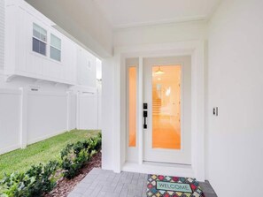 Une maison blanche avec une porte d’entrée, un paillasson et un petit jardin.