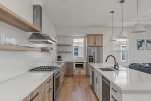 A modern kitchen with white cabinetry, stainless steel appliances, and wooden flooring. - White Sands Retreat - Pool/Hot Tub/Walk to Beach! (St. Augustine Beach)