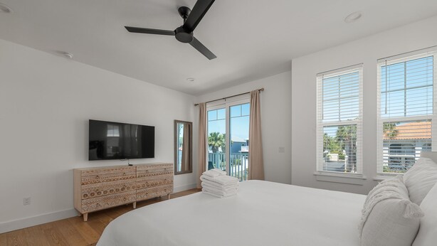 A bedroom with a bed, a TV, a dresser, and a ceiling fan. - White Sands Retreat - Pool/Hot Tub/Walk to Beach! (St. Augustine Beach)