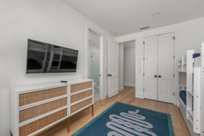 Een gang met een televisie, witte deuren, een console tafel met manden en een blauw vloerkleed.