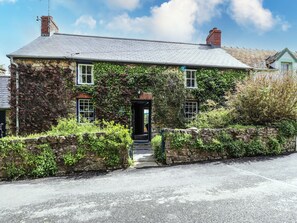 A stone house with ivy-covered walls, a tiled roof, and a small porch. - Tyddyn Bach (Newport)