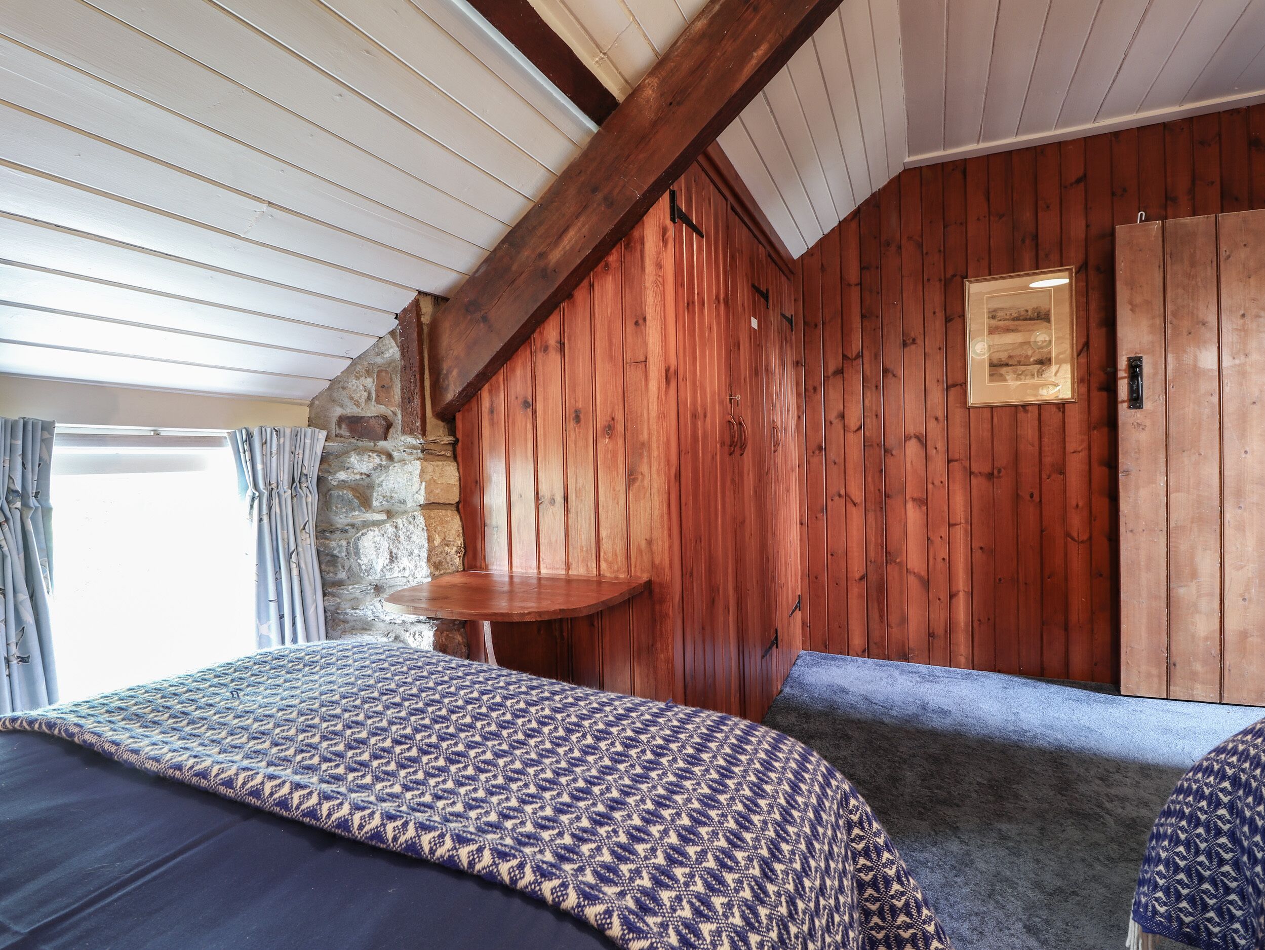Een kamer met een bed, een bankje, een houten wand en een ingelijste foto.