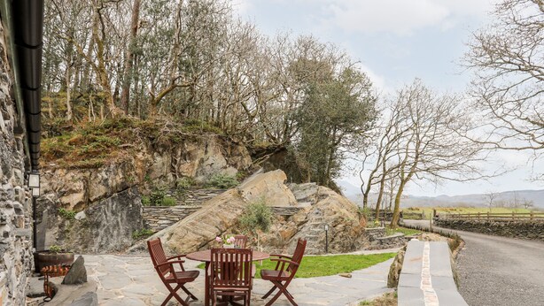 Eine Steinterrasse mit Tisch und vier Stühlen, umgeben von einer Steinmauer und Blick auf eine Berglandschaft.
